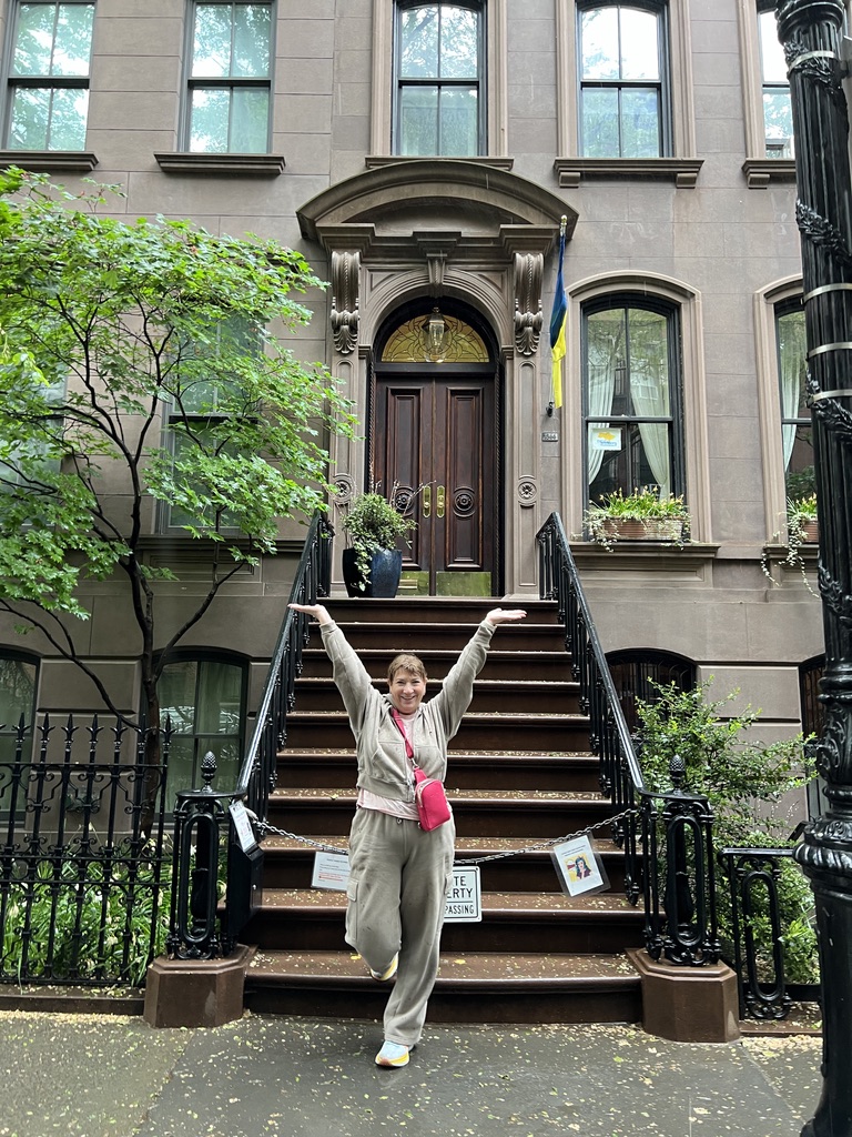 Michele Schwartz in a sweatsuit standing in pouring rain on the steps of a New York brownstone
